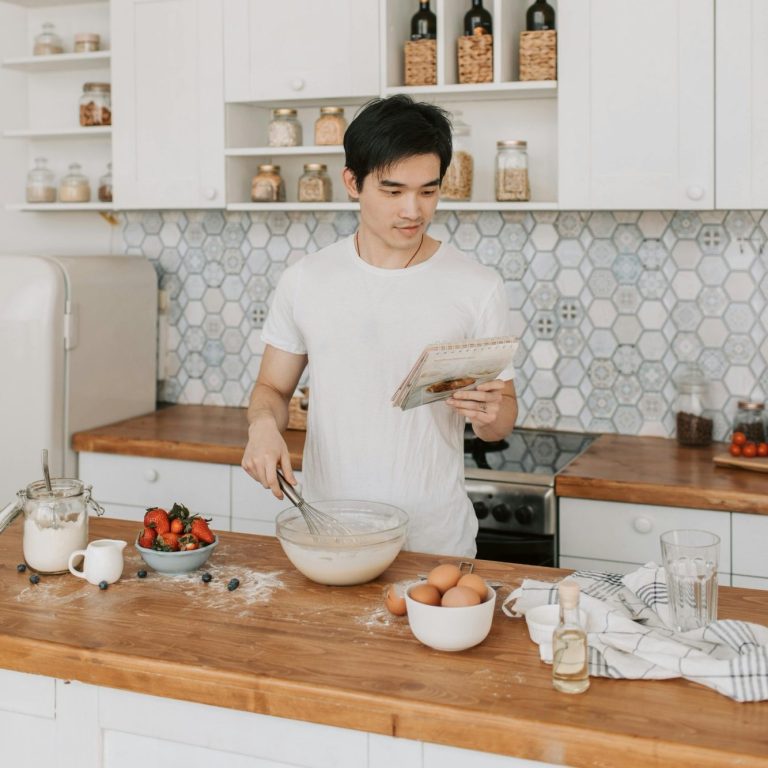 Backbuch für Hundeleckerchen Ein Mann bereitet Teig in einer modernen Küche mit frischen Zutaten vor und hat ein Rezept in der Hand.