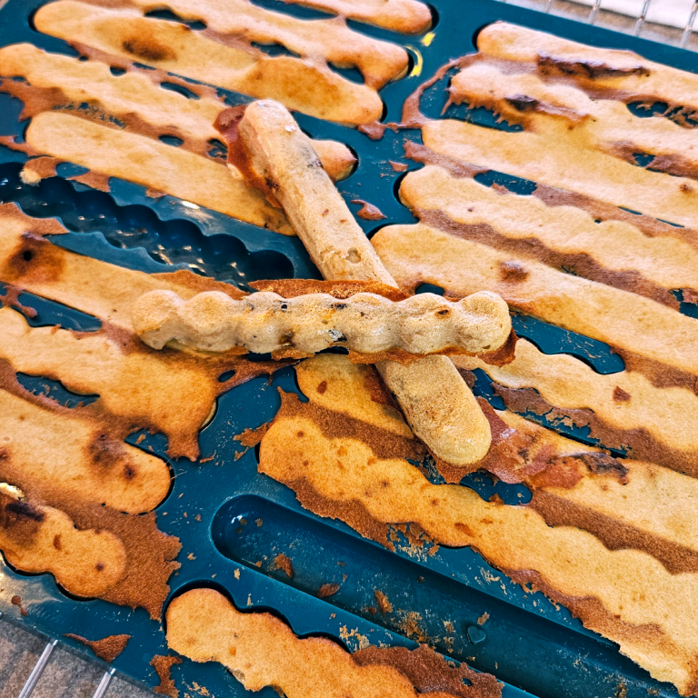 Eine blaue Backmatte von collory für Kaustangen mit Leckerchen dadrin. Eine Kaustange liegt oben drauf.