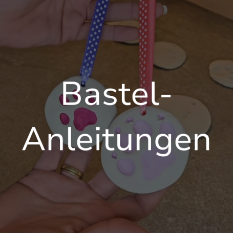 Link zur Seite "Bastelanleitungen". Auf dem Bild: Eine Hand hält zwei Anhänger mit Pfoten drauf.